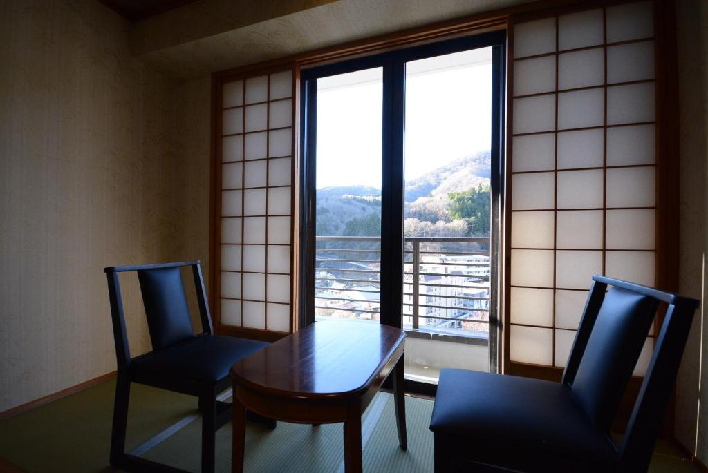 那須塩原市にある那須塩原　一萬亭のテーブルと椅子2脚、窓が備わる客室です。