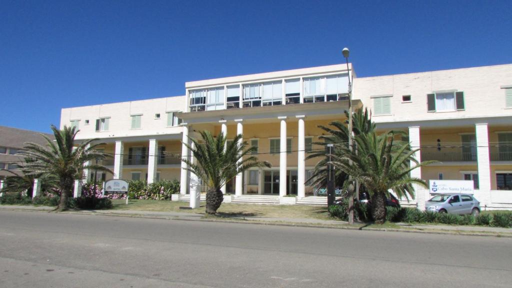 a large white building with palm trees in front of it at Hotel Cabo Santa Maria in La Paloma