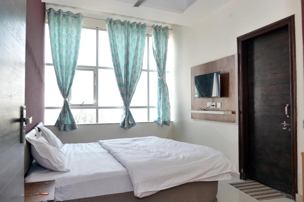 a bedroom with a bed and a window with blue curtains at HOTEL IRA Mansarovar Jaipur in Jaipur