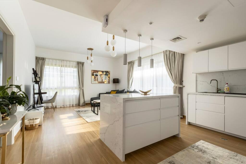 a kitchen with white cabinets and a living room at Bright & Relaxing 1BR Apartment in Dubai