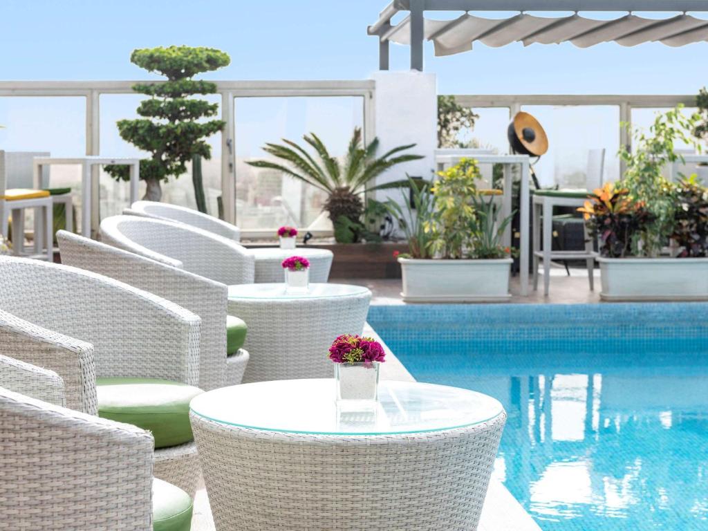 فندق موڤنبيك الدار البيضاء في الدار البيضاء: مجموعة من الكراسي البيضاء والطاولات بجوار حمام السباحة