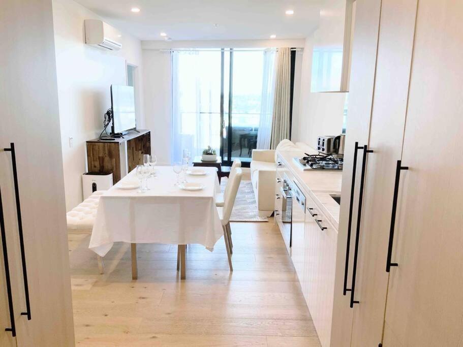 a white kitchen with a white table and a dining room at M-city Apartment - Executive Twin King Ensuites - Fully equipped - Free Parking, fast Wifi, smart TV, Netflix, complementary drinks & amenities - M-city shopping centre Clayton 3168 in Clayton North