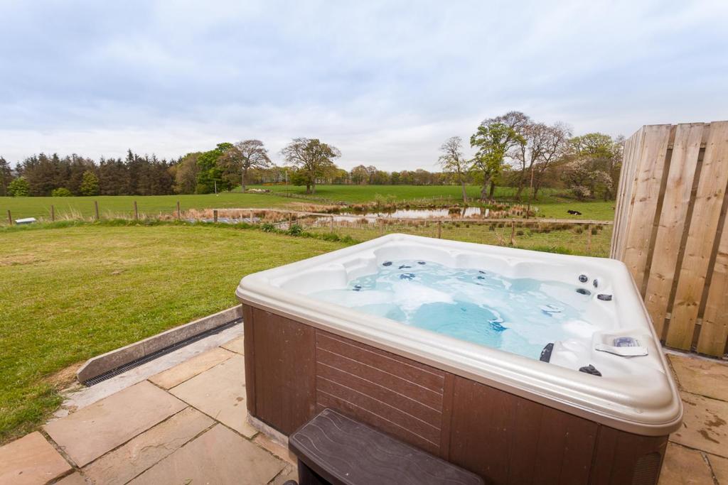 a hot tub in a yard with a field at 2 Eden at Williamscraig Holiday Cottages in Linlithgow