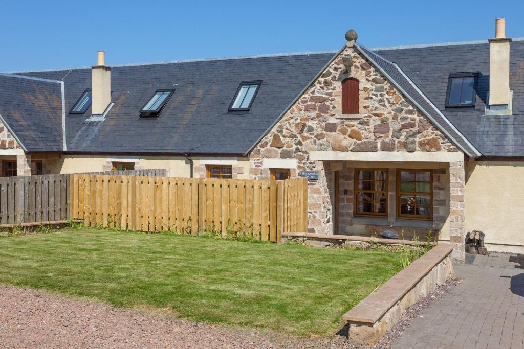 a house with a wooden fence and a yard at Honeysuckle Cottage at Williamscraig Holiday Cottages in Linlithgow