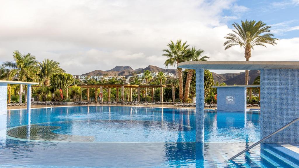 einen Pool in einem Resort mit Palmen und Bergen in der Unterkunft Playitas Aparthotel - Sports Resort in Las Playitas