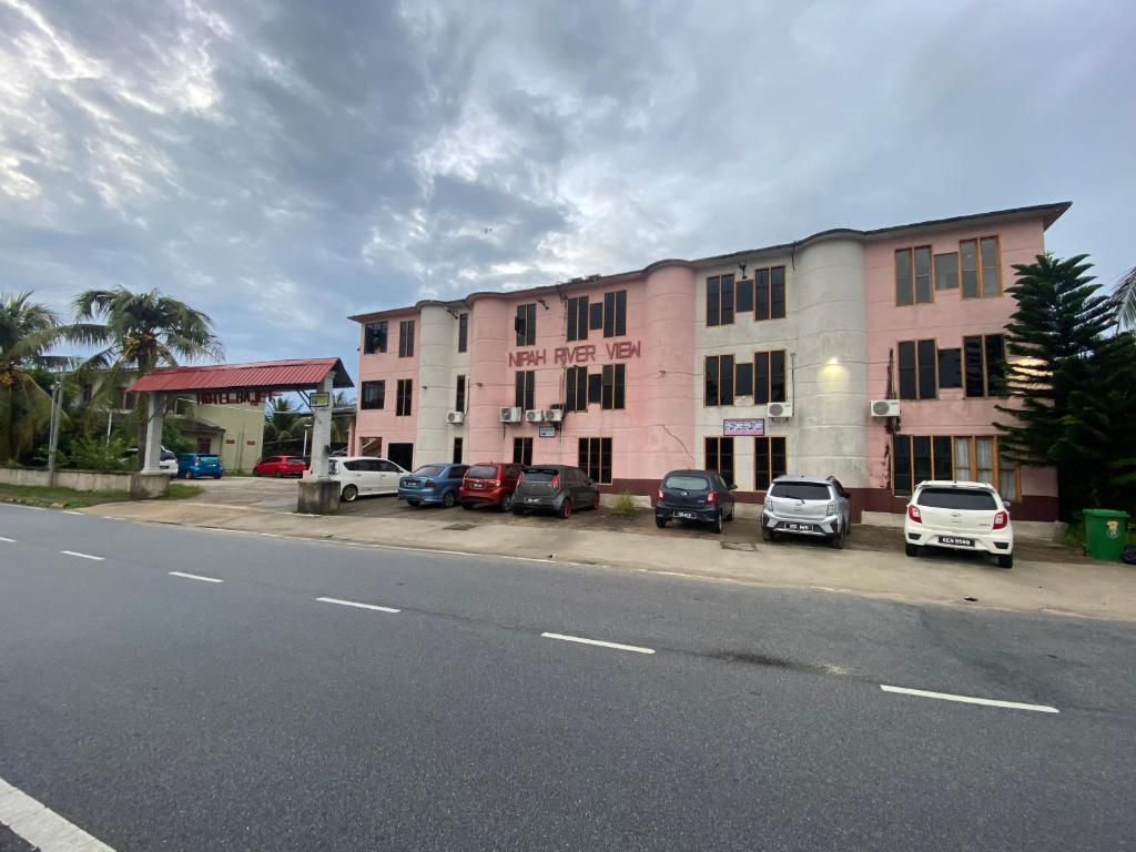 a street with cars parked in front of a pink building at Nipah River View Bajet Hotel in Kuala Terengganu