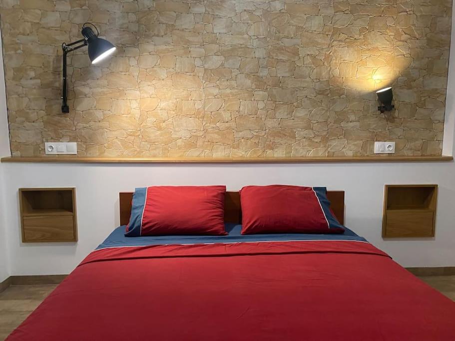 a bed with two red pillows and a stone wall at Central cozy apartment with garden in Alexandroupoli