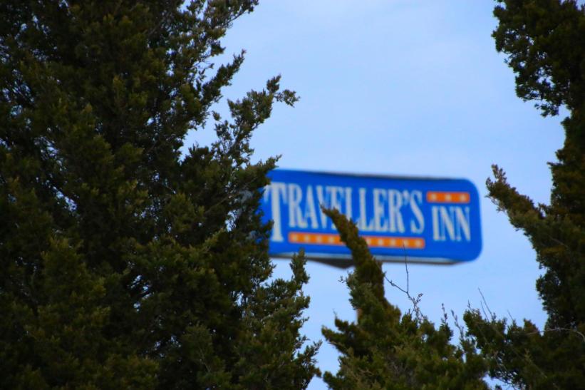 un panneau bleu indiquant une auberge en bois entre deux arbres dans l'établissement Travelers Inn Topeka, à Topeka