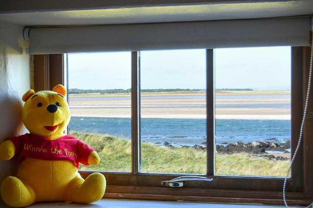 un ours en peluche jaune assis sur un rebord de fenêtre dans l'établissement Heather Cottages - Godwit, à Bamburgh