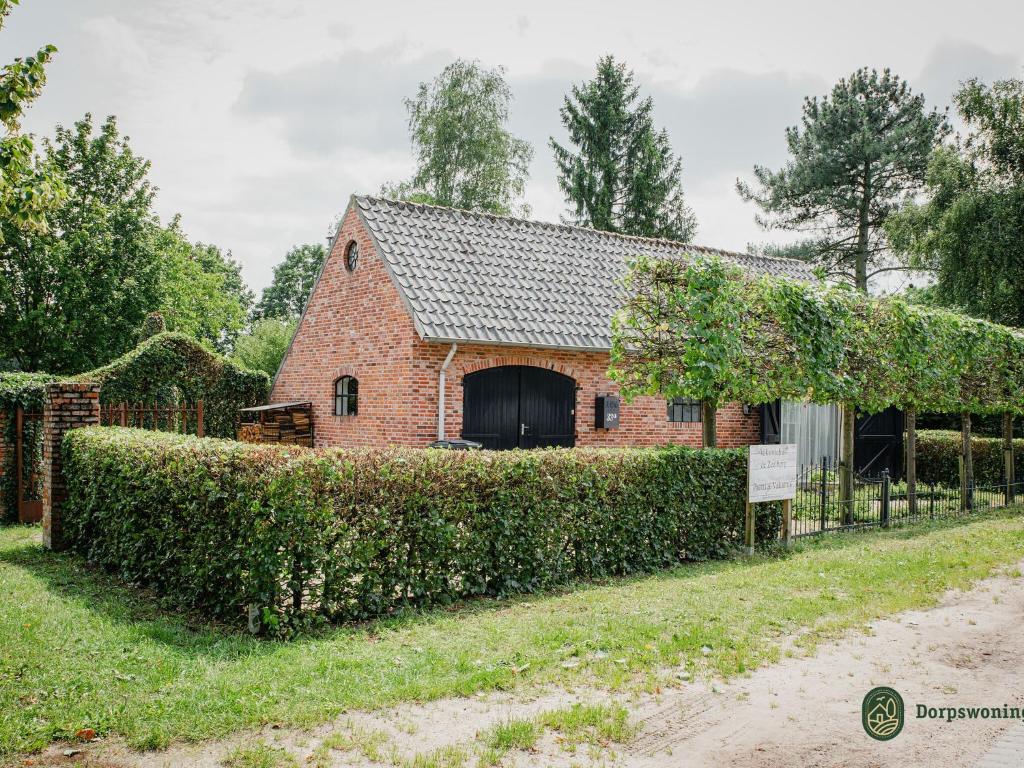 un antiguo granero de ladrillo con un seto delante de él en de Zeelberg, en Valkenswaard