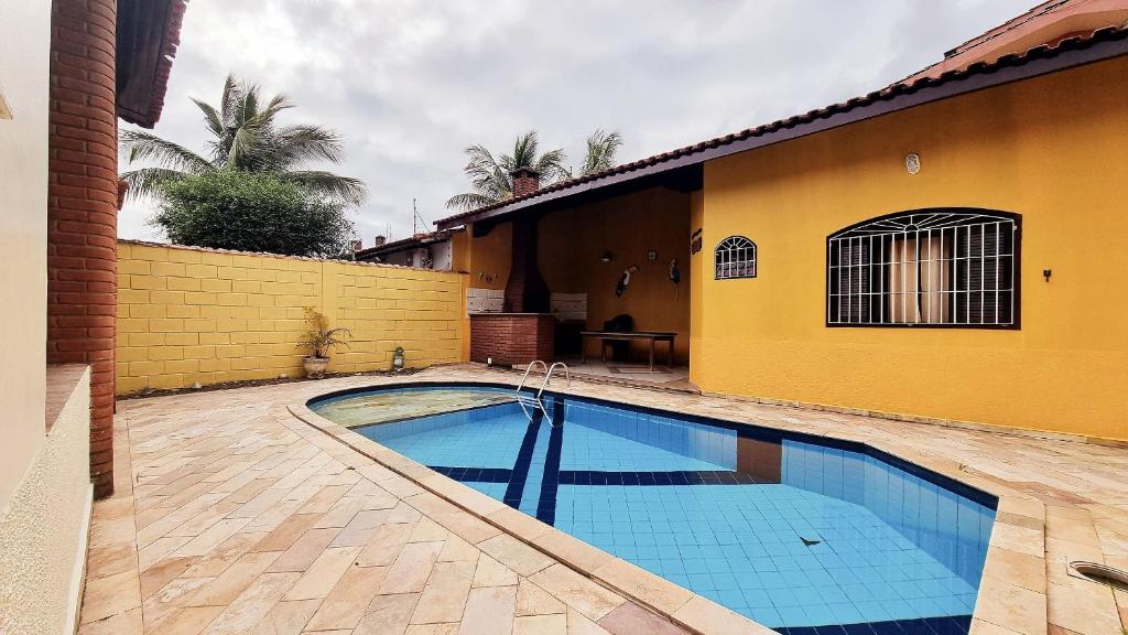 a swimming pool in front of a house with a yellow wall at Piscina, Churrasqueira, Wi-Fi, SmartTv, 4dorm, Comércios na porta in Itanhaém