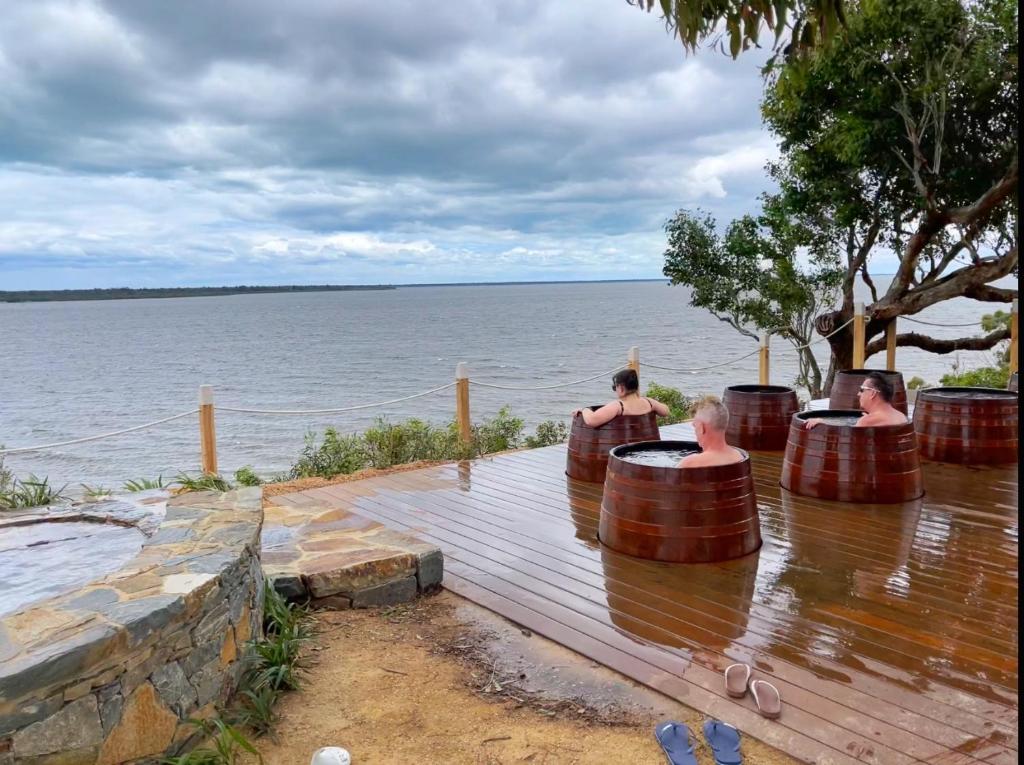 a group of people sitting in barrels on a wooden deck near the water at Luxury 3BR Hot Spring Retreat with KING Bed - Metung in Metung