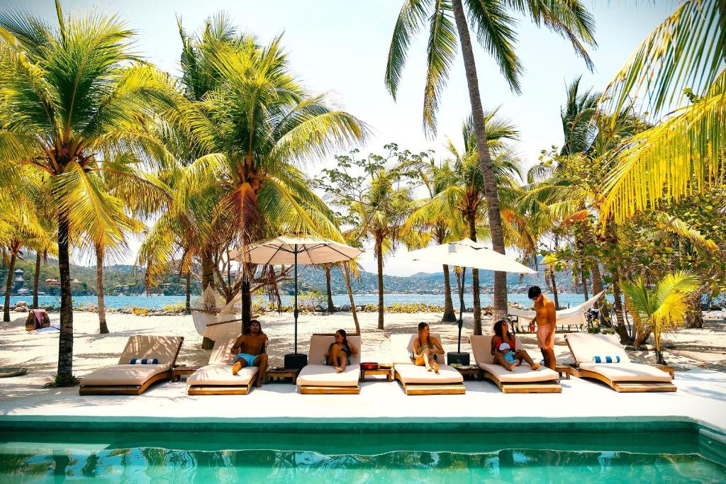 a group of people sitting on lounge chairs next to a pool at Casa Las Gatas in Zihuatanejo