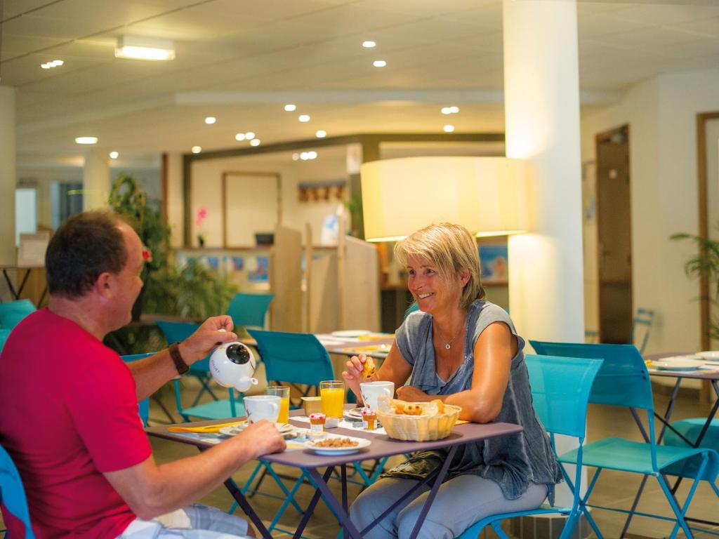 a man taking a picture of a woman sitting at a table at Résidence Vacances Bleues Les Jardins d'Arvor in Bénodet