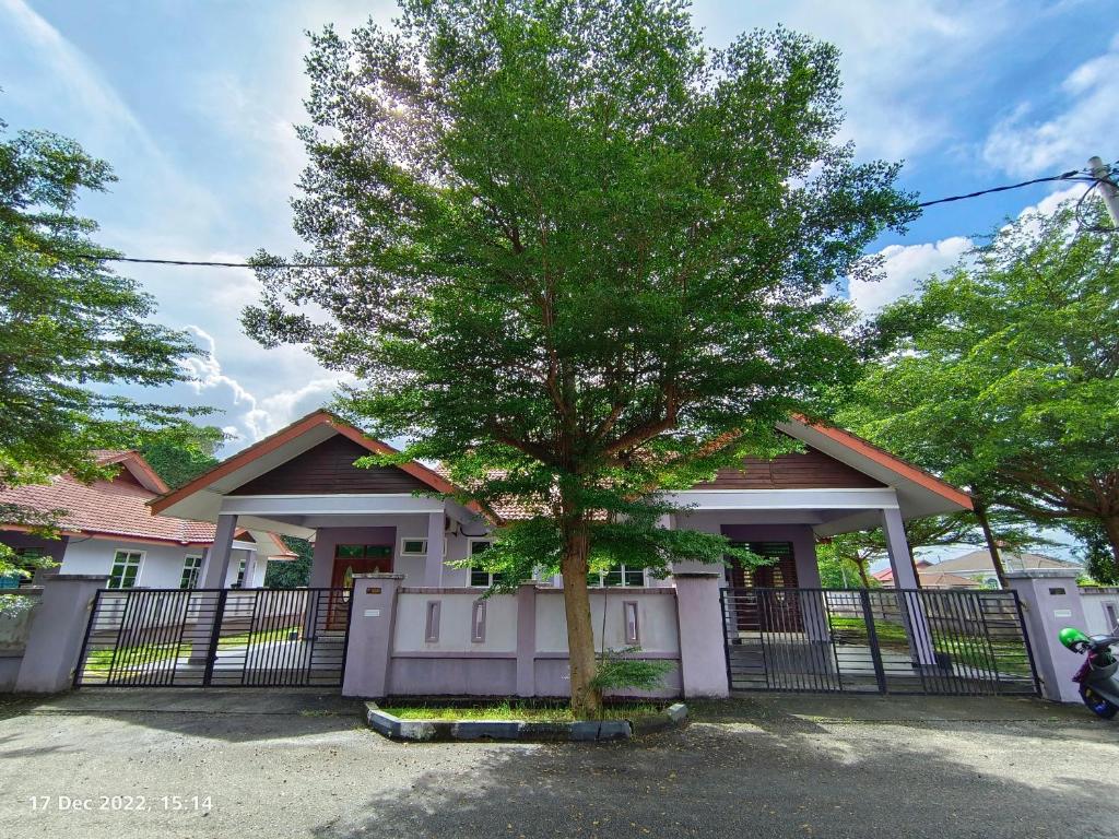 a tree in front of a house with a fence at Seri Guesthouse Dungun in Kampong Sura Masjid