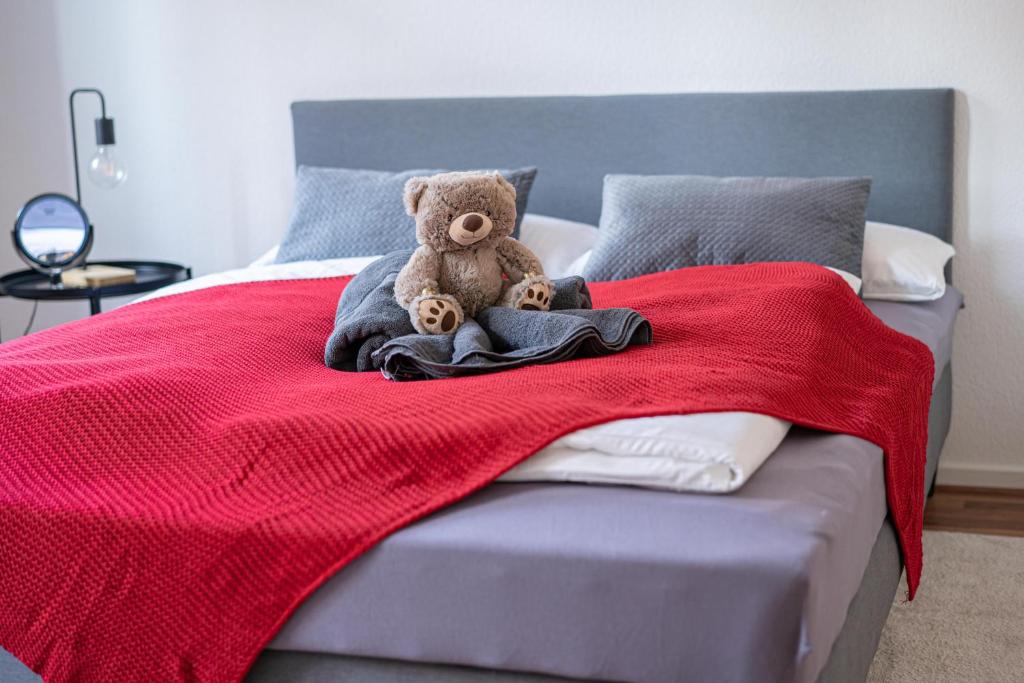 um urso de peluche sentado numa cama com um cobertor vermelho em FULL HOUSE Premium Apartments Magdeburg E3 em Magdeburg