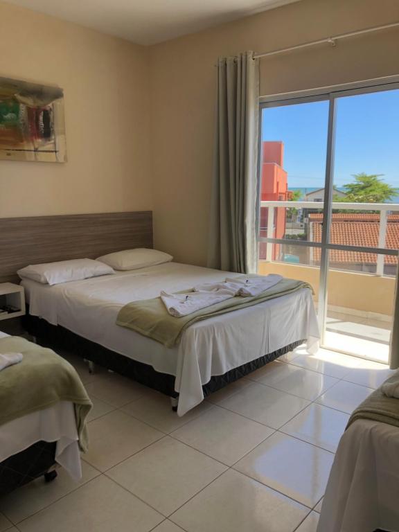 a bedroom with two beds and a large window at Perequê Praia Hotel in Porto Belo