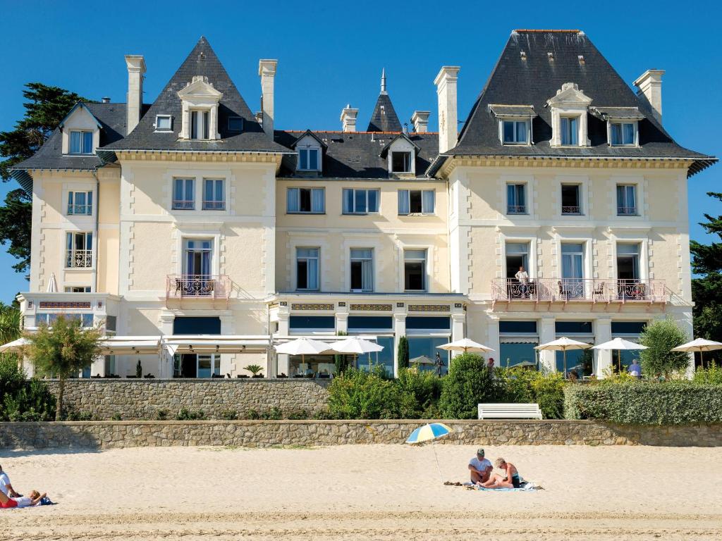 pessoas sentadas na praia em frente a uma casa grande em Hôtel Vacances Bleues Villa Caroline em La Baule