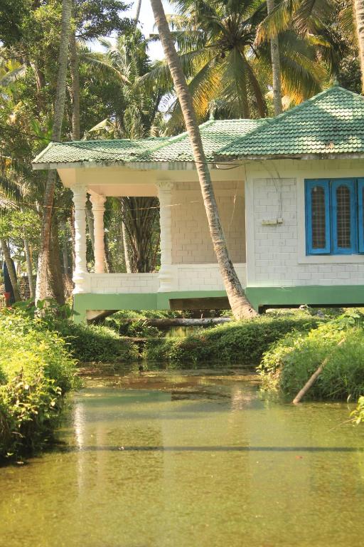 a small white house with blue windows next to a body of water at The Temple Tree Varkala in Varkala
