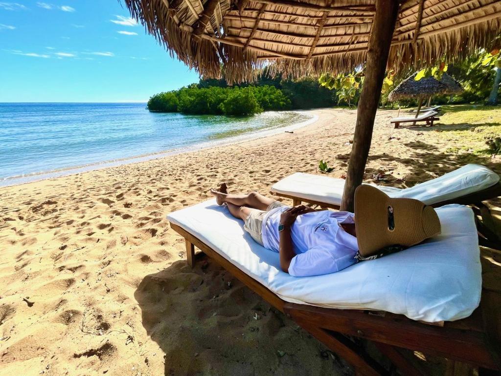 a person laying on a bed on a beach at Hotel Océan Beach Sakatia in Nosy Be