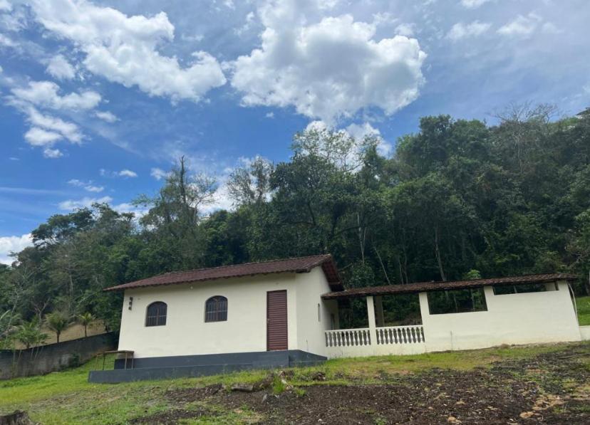 una pequeña casa blanca en un campo con árboles en Chalé em Pousada Recanto MD, en Itaboraí