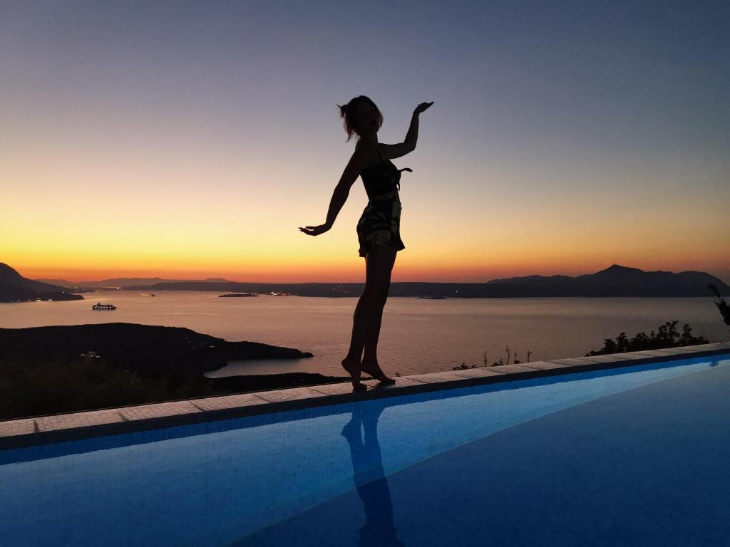 Una donna è in piedi sul bordo di una piscina di Villa Cassandra - A breathtaking view of Souda-Chania bay and the White Mountains a Kókkinon Khoríon