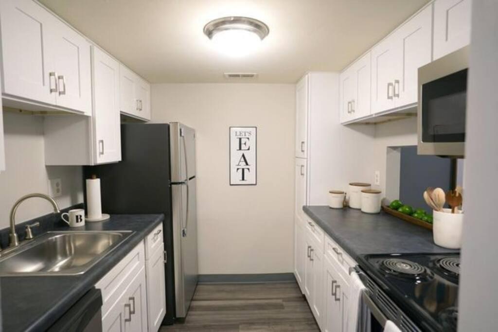 La cuisine est équipée de placards blancs et d'un réfrigérateur en acier inoxydable. dans l'établissement Modern 1 BR APT w/ Pool, Tennis court, Wi-Fi, & AC, à Monroeville