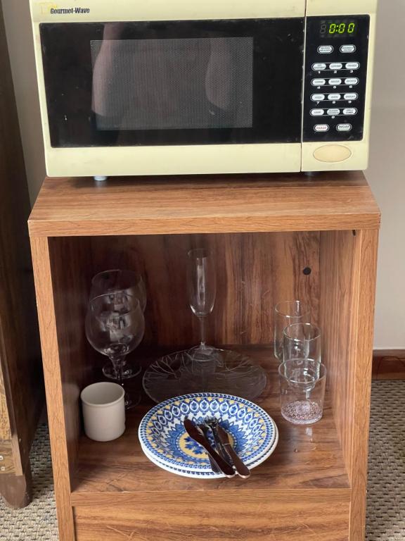 a microwave on a wooden stand with plates and glasses at PROMOÇÃO EXECUTIVA COM BANHEIRA E FLATS SEM BANHEIRA- Melhor Hotel De Taguatinga in Taguatinga