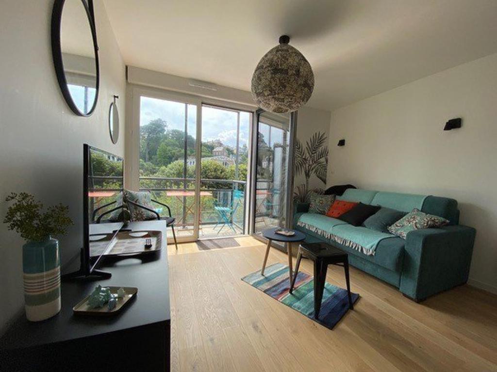 un salon avec un canapé bleu et une grande fenêtre dans l'établissement Appartement rénové avec balcon, parking et accès direct à la plage de Trestraou - Perros-Guirec - FR-1-368-260, à Perros-Guirec
