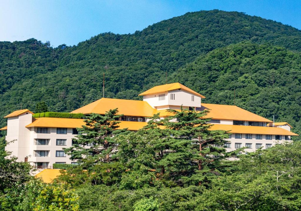 a large building with trees in front of a mountain at Hotel Koyokan in Hanamaki