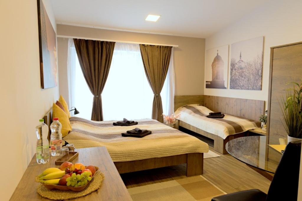 a hotel room with two beds and a table with a bowl of fruit at eHotel Esztergom in Esztergom