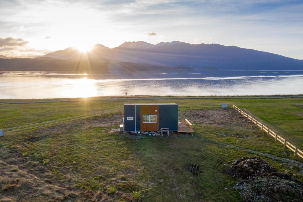 a small house on a field next to a body of water at Tiny Piece of Paradise - Te Anau Tiny House in Te Anau