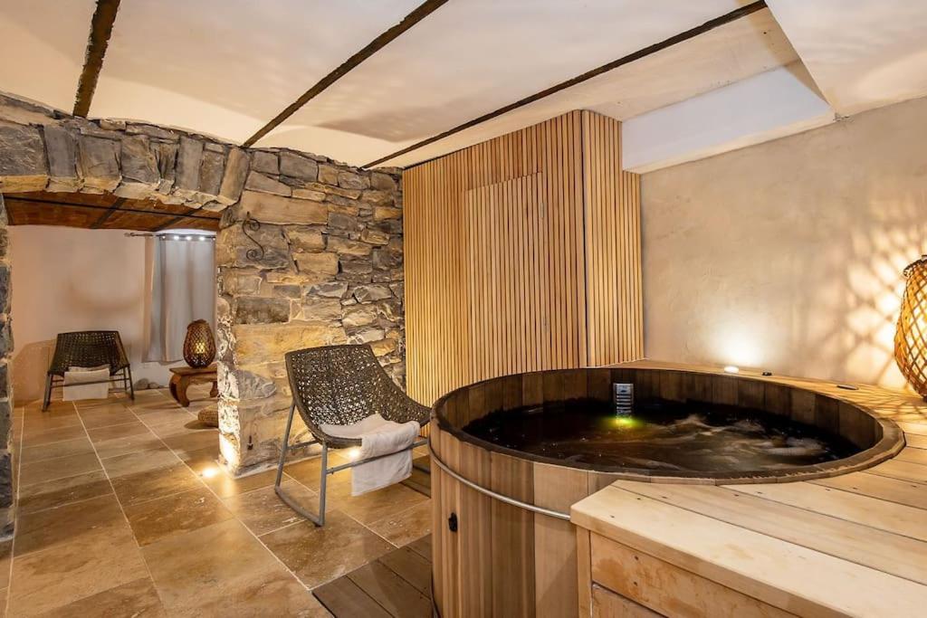 bañera de hidromasaje en una habitación con pared de piedra en Hébergement Deluxe avec Grand Jacuzzi et Sauna Millau, en Millau