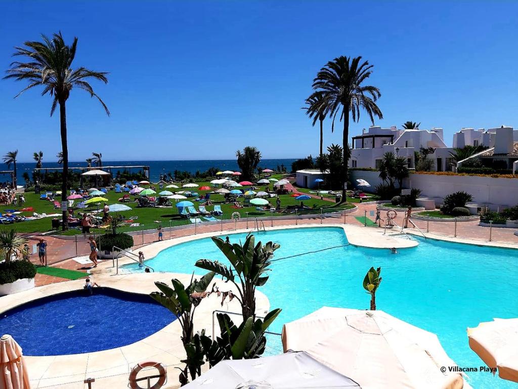 a large swimming pool with umbrellas and the ocean at Villacana Playa Silvia in Estepona