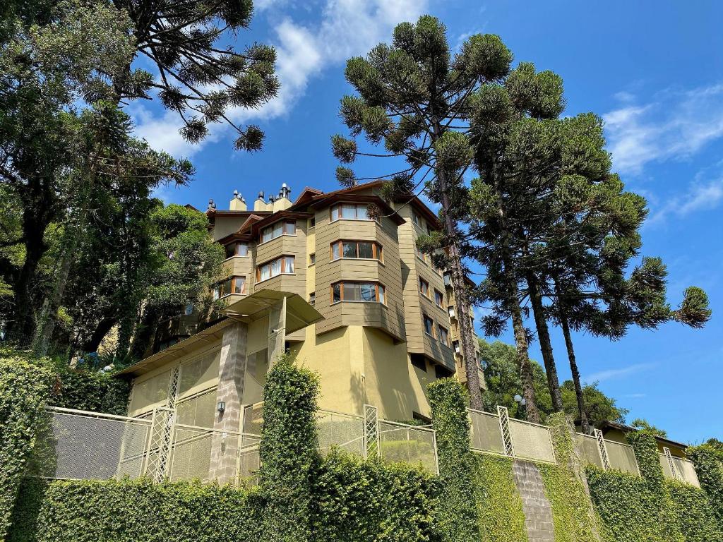 a building on a hill with a fence and trees at Apartamentos Lagos de Gramado by Achei Gramado in Gramado