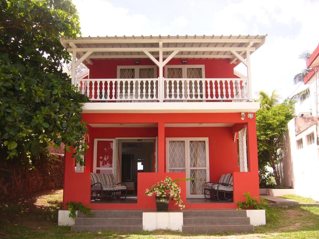 une maison rouge avec un balcon blanc au-dessus dans l'établissement Colibri Beach Villas, à Trou dʼ Eau Douce