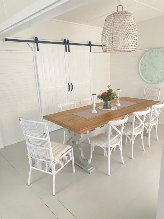 uma mesa de jantar com cadeiras brancas e um relógio em Stay Salty em Culburra Beach