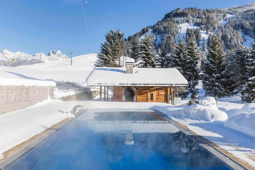 a swimming pool covered in snow in front of a house at Hotel Hohenfels in Tannheim