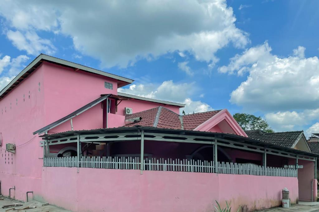 uma casa cor-de-rosa com uma varanda em RedDoorz near Simpang Bandara SMB II em Palimbão