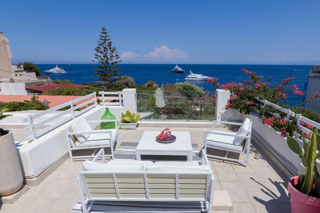 un patio con sillas blancas, una mesa y el océano en Villa Sea Rose, en Lipari