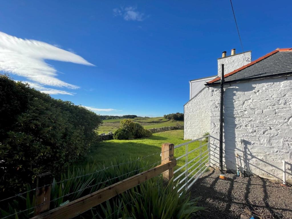 a house with a fence and a field in the background at Pass the Keys Beautiful 5BR Rural Cottage with Outstanding Views in Castle Douglas