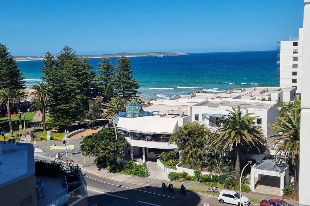 a building on a street with the ocean in the background at Spectacular Waterfront Views Discover the Hidden Gem of Cronulla with our Rare 3 Bedroom Apartment with Free Parking in Cronulla