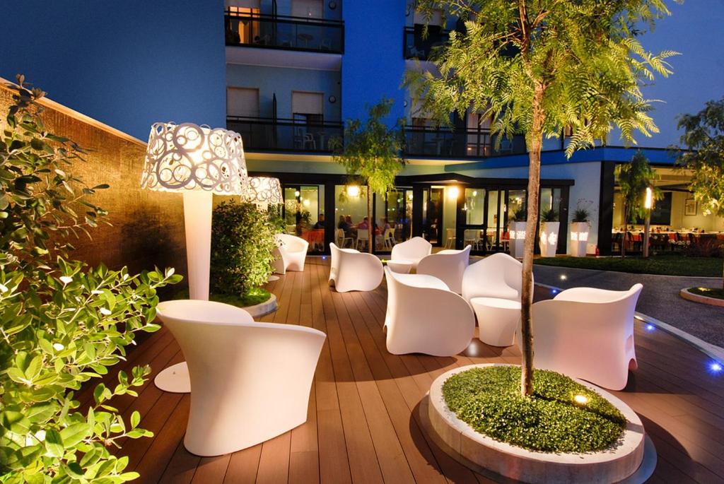 un patio avec des chaises blanches, un arbre et un bâtiment dans l'établissement Hotel Continental, à Tortoreto Lido