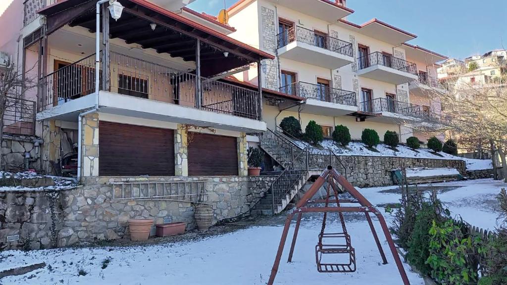 une aire de jeux en face d'un bâtiment dans la neige dans l'établissement Ξενώνας Μενελαΐς - Menelais Apartments, à Thrapsímion