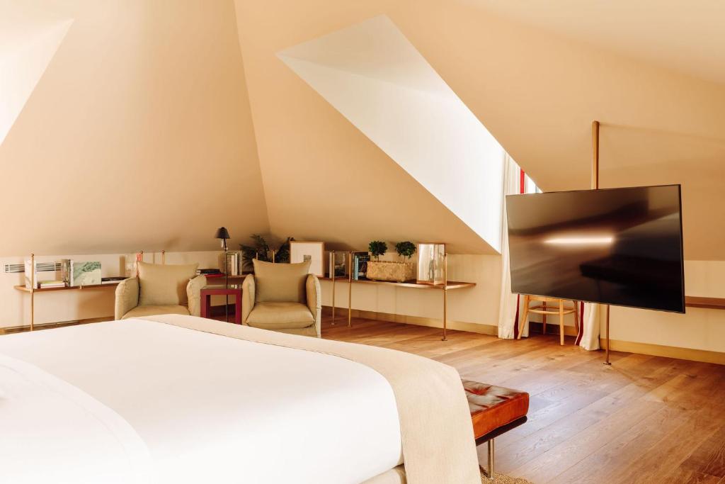 A spacious attic-style bedroom with lounge chairs, shelving, and a large television.