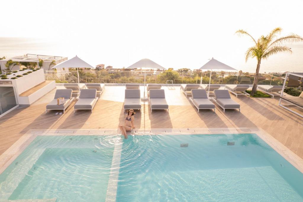 uma piscina com espreguiçadeiras e o oceano em Midenza Seaside & Nature Retreat em Capo Vaticano