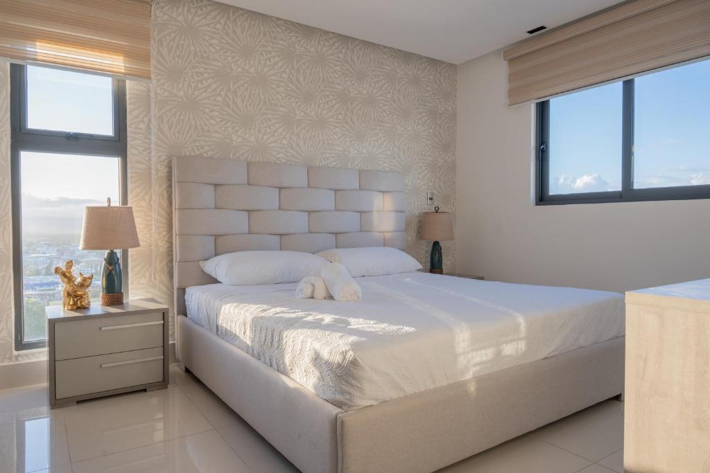 a white bedroom with a large bed and two windows at Top Floor in Luxury Tower in Santiago de los Caballeros