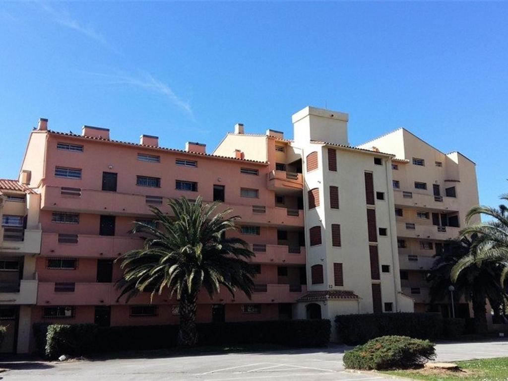 un grand bâtiment avec des palmiers devant dans l'établissement Appartement T2 à Argelès-sur-Mer, plage à 300m, piscine, parking privé, animaux acceptés - FR-1-388-109, à Argelès-sur-Mer