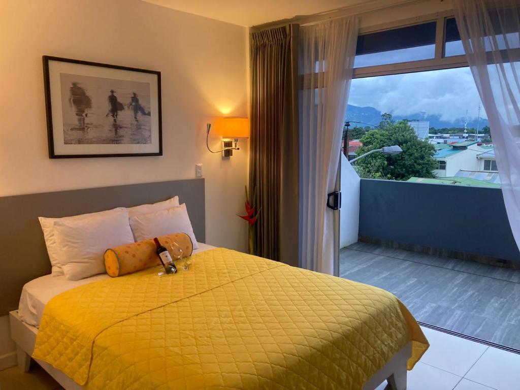 1 dormitorio con cama amarilla y balcón en Apartahotel Altos de la Sabana, en San José