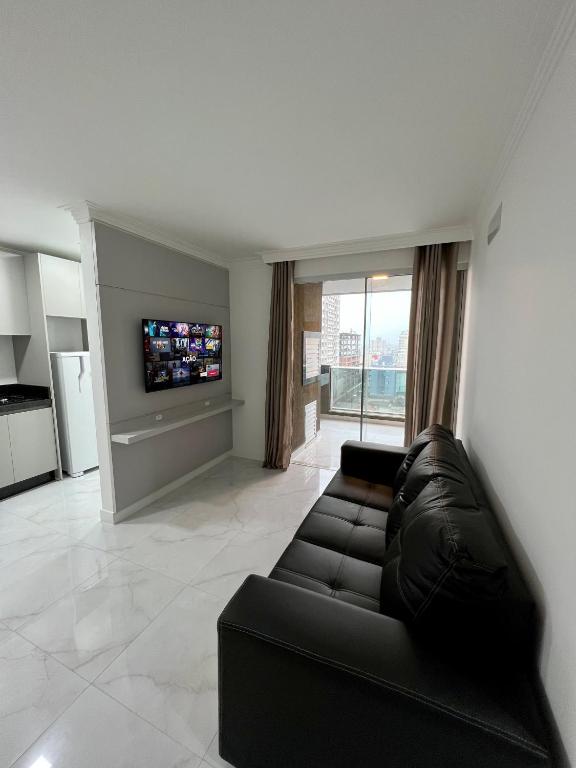 sala de estar con sofá negro y TV en Apartamento próximo à praia, en Itapema